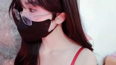 Media: Video of an Asian woman with long black hair, wearing a black face mask, red spaghetti strap top, and clear glasses, against a textured grey background.