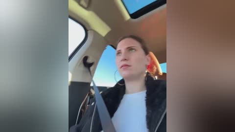 Media: Video of a woman with fair skin and brown hair, wearing a black jacket, looking out the window of a car.