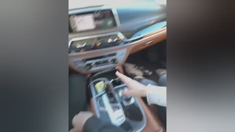 Media: A video shows a close-up of a person's hands shifting a car's gearstick. The vehicle's interior features a modern dashboard with a steering wheel and speedometer. The scene is blurry, with a focus on the hands and gearstick.