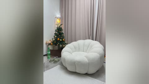 Media: Video of a cozy living room with a plush white beanbag chair, a decorated Christmas tree, beige curtains, and a green plant on the floor.