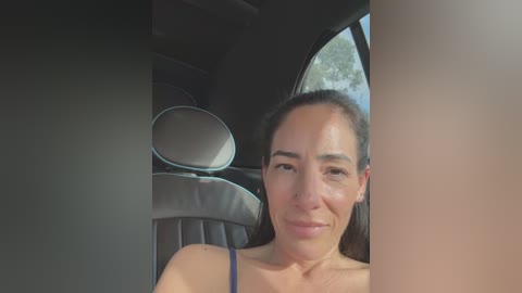 Media: Video of a smiling woman with light brown skin and long dark hair, seated in a car with black leather seats, window partially covered by a black object.