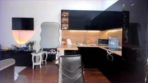 Media: A modern, minimalist kitchen with black cabinets, wooden countertop, and sleek stainless steel appliances. A black leather chair and a white side table with a vase are in the foreground.