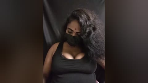 Media: A video of a Black woman with medium skin tone, wearing a black mask, black tank top, and long black hair, against a dark background.