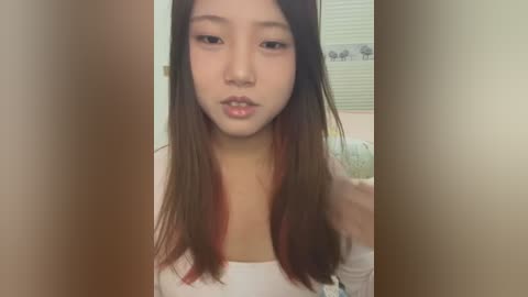 Media: Video of an Asian woman with long, straight black hair and fair skin, wearing a white top, standing in a bathroom with a window and shower curtain visible in the background.