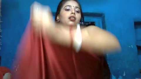 Media: A blurred video of a South Asian woman with dark skin, wearing a red sari, captured in a dimly lit room with blue lighting.