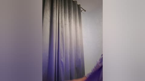 Media: A video of a minimalist bathroom with a gray curtain partially drawn, revealing a small, dimly lit room with a white wall and a faint purple light source.