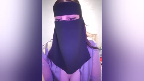 Media: Video of a woman with light skin and long brown hair, wearing a black niqab covering her face, and a white shirt with a visible cleavage, in a dimly lit room.