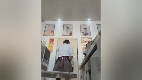 Video of a Japanese-style restaurant with a woman in a white shirt and gray skirt facing away, viewed from the back. The walls are adorned with vintage posters and menus.