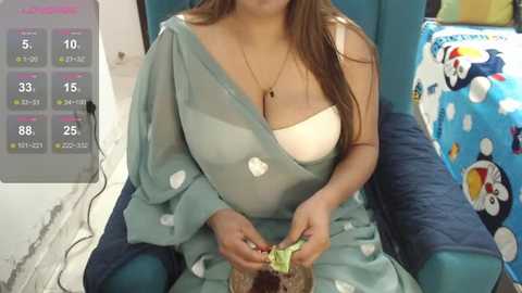 Media: A video of a South Asian woman with long brown hair wearing a light blue saree and white bra, seated on a blue cushioned chair. She is holding a small green leaf in her hands.