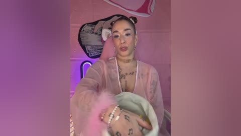 Media: A video of a tattooed woman with a pink hairdo, wearing a sheer pink top, holding a pink balloon in a dimly lit, pink-walled room.