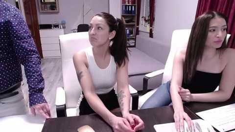 Media: Video of two Asian women in office attire, sitting at a conference table, discussing papers. The background shows a modern office with bookshelves and a white chair.