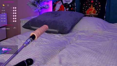 A video of a dimly-lit bedroom with a grey cushion on a white bedspread, a man using a microphone on a stand, and a colorful wall poster featuring a castle.