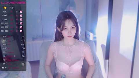 Media: A video of an East Asian woman with long black hair, wearing a sheer pink top, sitting in a dimly lit room. The image includes a screen overlay with chat icons and a timestamp.