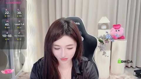 Media: Video of a young woman with long black hair, wearing a black jacket, sitting in a black gaming chair, surrounded by gaming equipment and plush toys, with a live stream overlay.