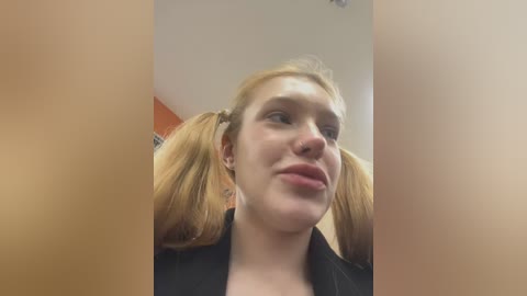 Media: Video of a young woman with fair skin and blonde pigtails, wearing a black jacket, making a pouty face. Background is blurred.