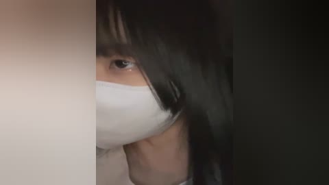 Media: Video of a young woman with long black hair, wearing a white face mask, partially visible in the frame, dark background.