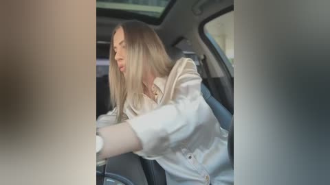 Video of a blonde woman in a white blouse, looking distressed, leaning out of a car window, blurred background.