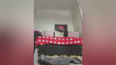 Media: A video of a cozy, themed bedroom with a red blanket adorned with white heart patterns, pink pillows, a black bedspread, and a red lipstick print on the wall.