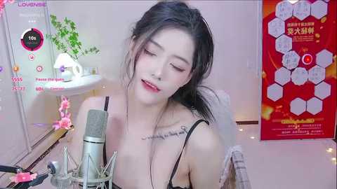 Media: Video of a young Asian woman with fair skin, dark hair, wearing a black bra, singing into a microphone, surrounded by pink flowers and a red poster.