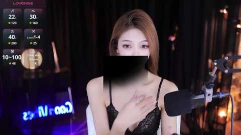 Media: A video of an Asian woman with shoulder-length brown hair, wearing a black lace bra, sitting in front of a microphone, with a blurred background.