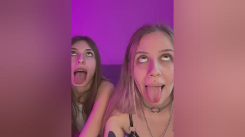 Media: Video of two young women with long hair, wearing tank tops, sticking out their tongues in a playful, exaggerated manner, with purple lighting.