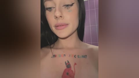 Media: A close-up video of a young woman with pale skin, black hair, and dark winged eyeliner. She has a tattoo of a red devil with a pitchfork on her chest, and a purple tiled bathroom background.