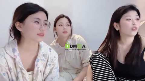 Media: Video of three East Asian women with light skin, dark hair, wearing casual clothes, sitting in a living room, looking serious.