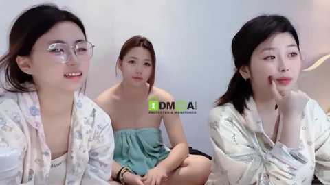 Media: Video of three East Asian women, one with glasses, sitting together in casual attire, in a simple indoor setting with a watermark.