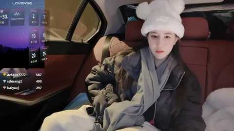 Media: Video of a young Asian woman in a fur hat and jacket, sitting in a car, with a weather app on the dashboard displaying snowy conditions.