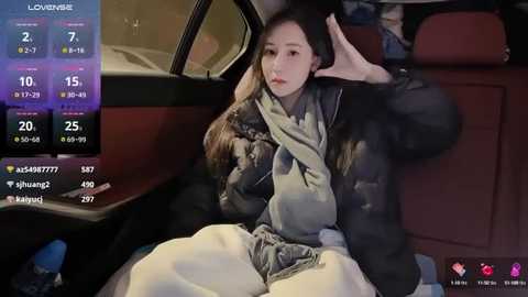 Media: A video captures a young woman with long black hair, wearing a black jacket and white pants, sitting in the backseat of a car, looking exhausted.