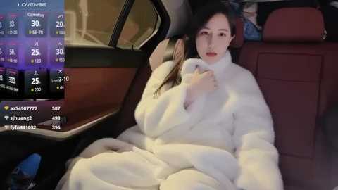 Media: Video of a young Asian woman in a fur coat, seated in a car with a temperature display, showing 26\u00b0C. She looks pensive, with a slightly open mouth.