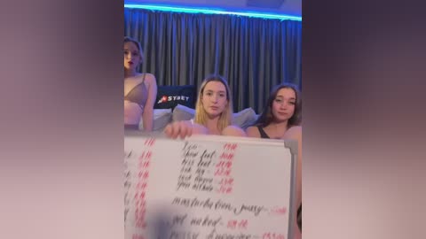 Media: Video of three young women in lingerie, holding a note listing sexual positions, in a dimly-lit room with blue lighting.