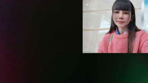 Media: Video of a young Asian woman with straight black hair, wearing a pink sweater and listening to headphones, indoors with blurred background.