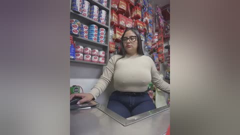 Media: A video of a plus-size Latina woman with glasses and long hair, wearing a tight beige top and high-waisted jeans, working behind a glass counter in a brightly lit convenience store stocked with colorful snacks.