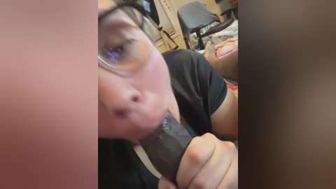 Media: Video of a person with fair skin and glasses performing oral sex on a large, erect penis. Background shows a messy room with office furniture.