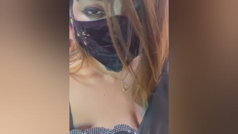 Media: Video of a woman with fair skin, wearing a black mask, green eye makeup, and a black top, her long red hair partially covering her face.