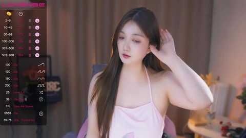 Media: Video of an East Asian woman with long black hair, wearing a pink halter top, adjusting her hair in a cozy room.