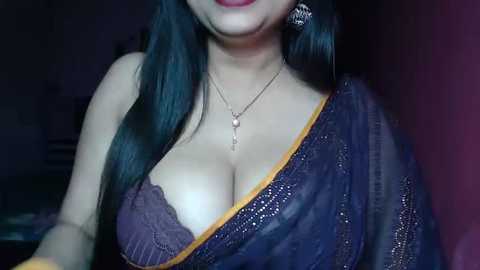 Media: Video of a woman with long, dark hair, wearing a purple saree with a yellow border, revealing her cleavage, and a gold necklace with a pendant.