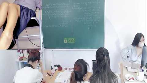 Media: A video of an Asian classroom with a teacher at a blackboard, students writing, and a teacher's legs visible in the corner.