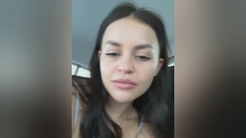 Media: A video of a young woman with long dark hair, fair skin, and minimal makeup, looking slightly downcast. She's in a car with a blurred background.