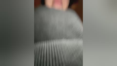 Media: A close-up video of a woman's upper torso, partially blurred, wearing a grey sweater with a ribbed texture, revealing her breasts. Her face is partially visible in the background, with short dark hair. The background is out of focus.