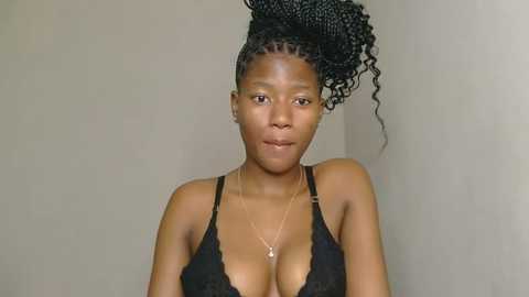 Media: Video of a young African woman with medium brown skin, wearing a black lace bra, her hair styled in a high, curly updo. She has a slender physique and small, natural breasts.