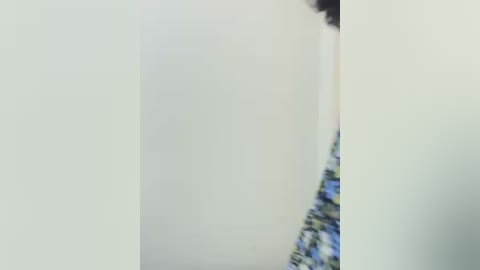 Media: A blurry video showing a person in a white dress, partially obscured, standing against a white background. The dress has a blue and green floral pattern.