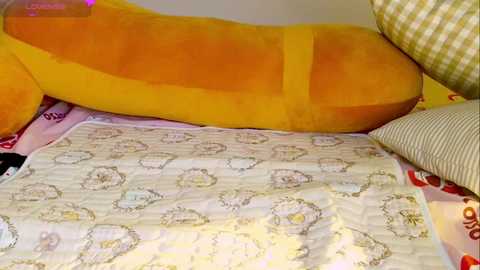 A video featuring a large, plush banana and a checkered pillow on a bedspread with pastel floral patterns. The background is a light-colored wall, and the room appears cozy and playful.