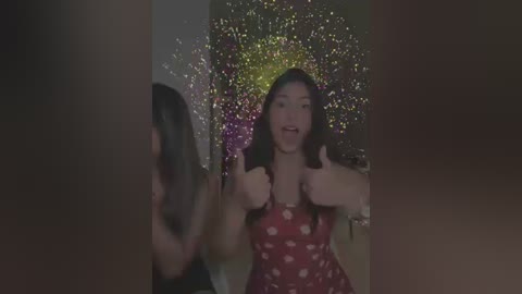 Media: A video captures a young woman with long brown hair, wearing a red polka-dot dress, giving a thumbs-up in a dimly lit room with a colorful confetti backdrop.