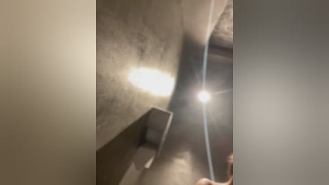 A video of a narrow, dimly lit corridor with a light source at the end, casting a bright beam on the right wall. The walls are gray and the floor appears to be concrete, giving the scene a slightly eerie, confined feel.