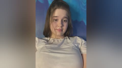 Media: A video of a young Caucasian girl with straight brown hair, wearing a white t-shirt, standing against a blue and purple gradient background.