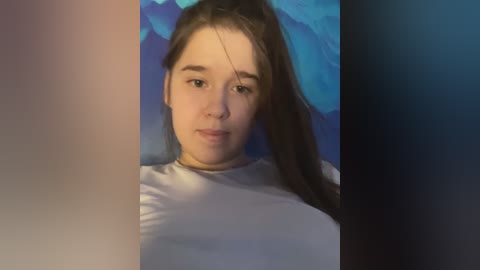 Media: Video of a young Caucasian woman with straight, long brown hair, wearing a white shirt, against a blue and black gradient background.