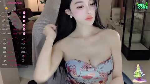 Media: A video of an East Asian woman with long black hair, fair skin, and a strapless floral dress, posing indoors in a modern room.