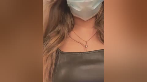 Media: A video of a person wearing a light blue surgical mask, a black leather strapless top, and a gold necklace. The background is a warm, gradient brown.